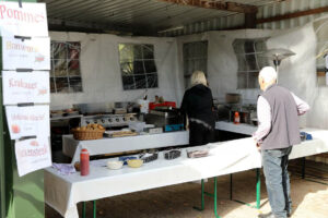 Ein Mann wartet vor einem Essensstand und die Frau im Hintergrund bereitet ihm mit viel Liebe seine bestellten Speisen vor.