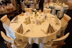 Elegant gedeckter Hochzeitstisch mit weißen Tischdecken und goldenen Servietten, der festliche Atmosphäre ausstrahlt.