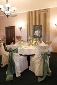 Eleganter Bankettsaal mit weißen Tischdecken und grünen Schleifen, der eine festliche Atmosphäre ausstrahlt.
