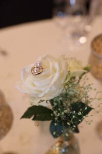 Eine elegante weiße Rose, geschmückt mit einem funkelnden goldenen Ring, der ihre Schönheit unterstreicht.